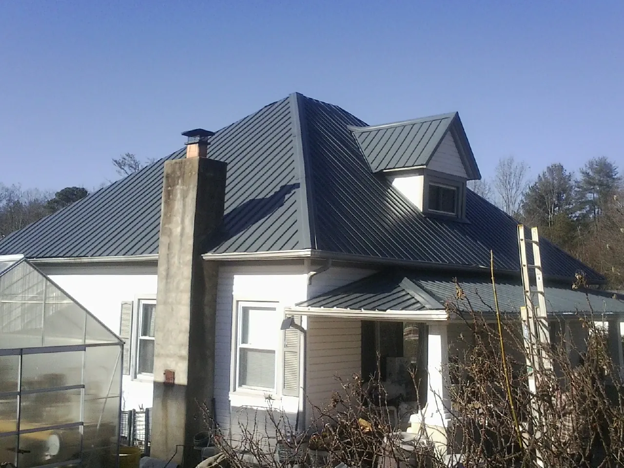 Dark blue standing seam metal roof on a white farmhouse with dormer — Slate & Tile Roof Repair by Roofing Brothers in Crompond