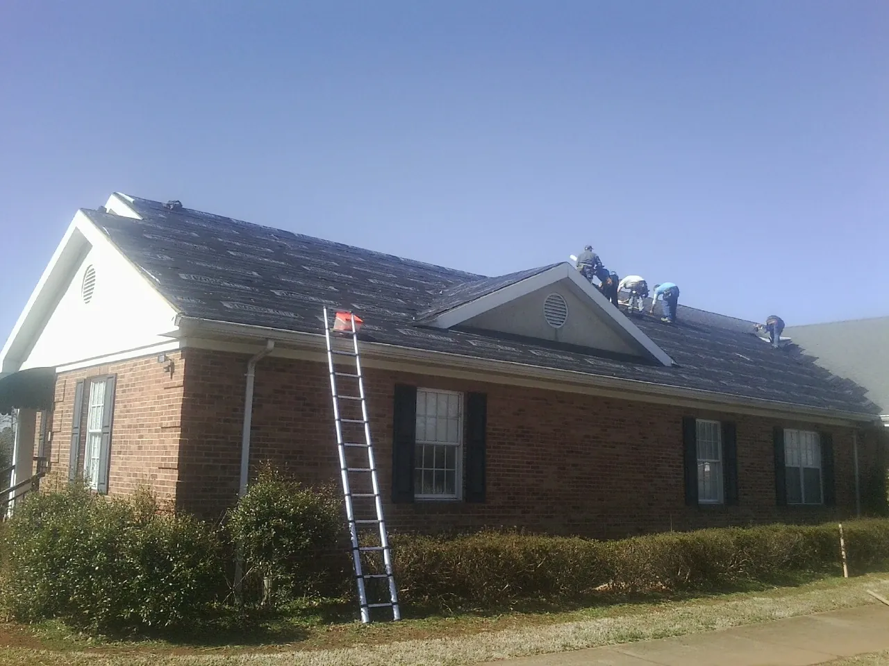 Crew tearing shingles off a brick ranch roof with a ladder set — Metal Roof Repair work by our crew in Crompond