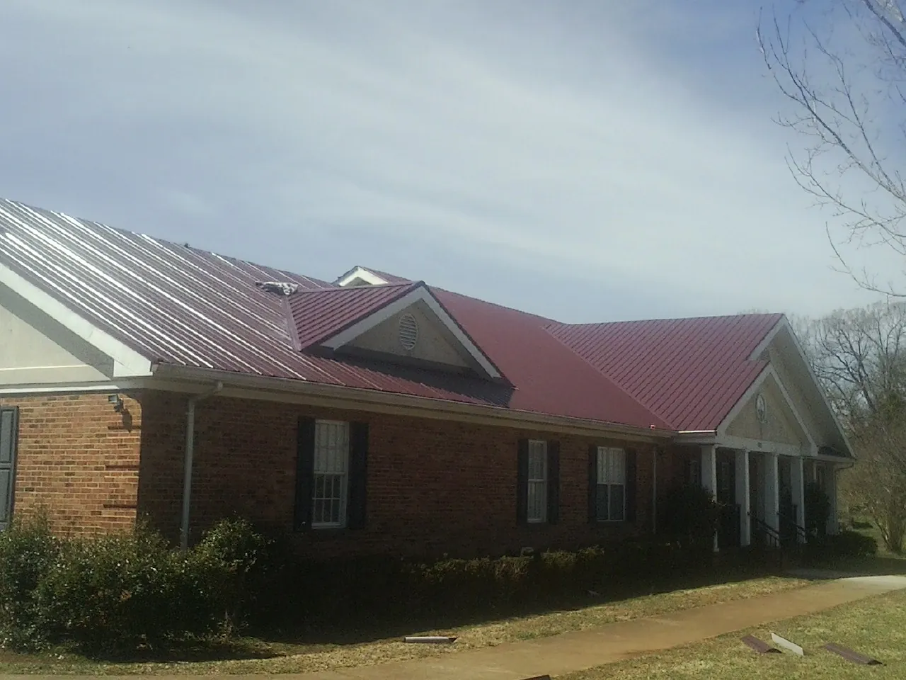 Red metal roof with gabled entries on a long brick building, from a Hail Damage Roof Repair job in Crompond
