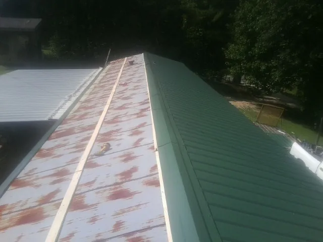 Old rusted panels beside newly installed green metal roofing — Wind Damage Roof Repair by Roofing Brothers in Crompond