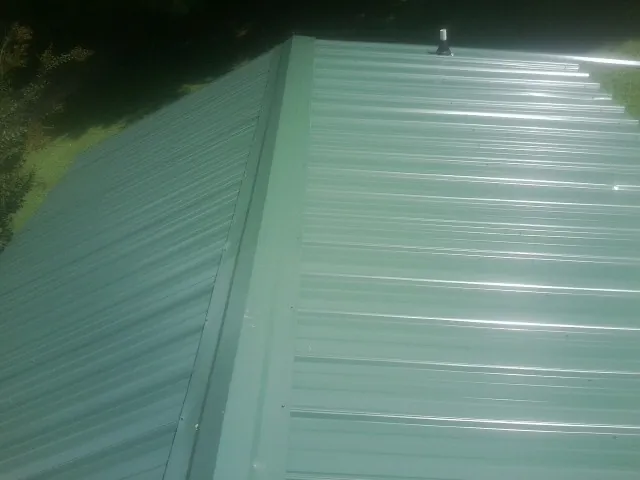 New green metal panels meeting at the ridge of a roof — Flat Roof Repair work by our crew in Crompond