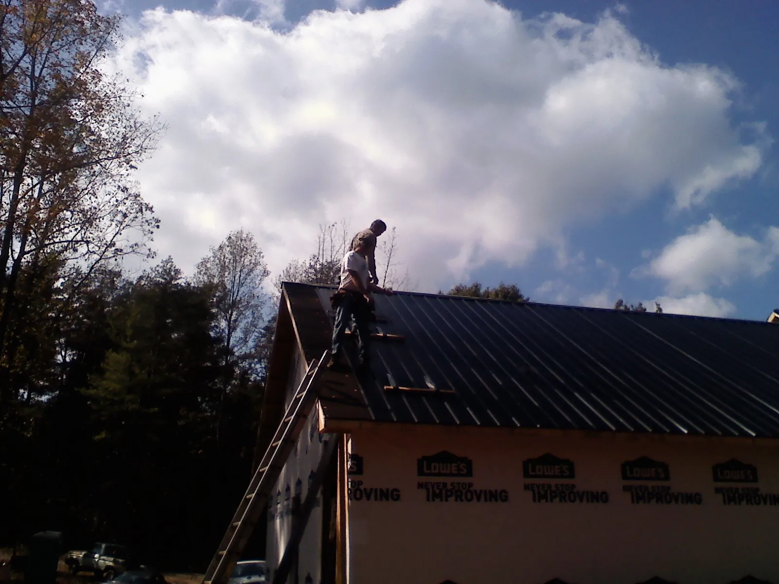 Roofer fastening dark metal panels high against a cloudy sky, from a Roof Inspection job in Crompond