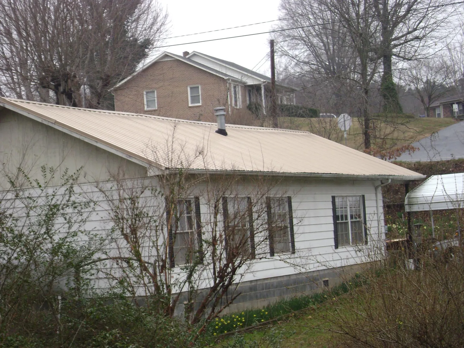 Tan metal roof on a white sided house set into a hillside — Commercial Roofing by Roofing Brothers in Crompond